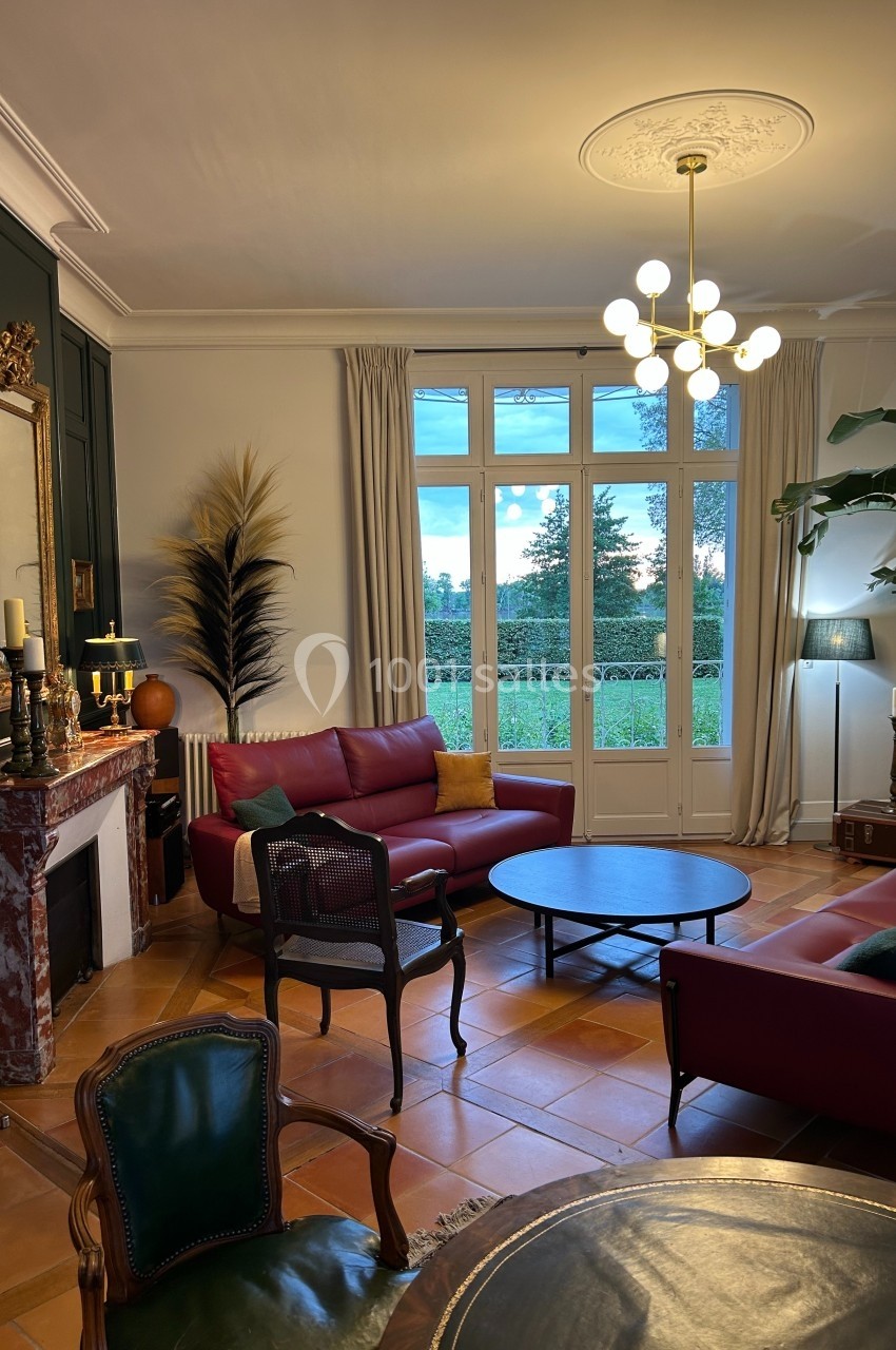 Salon élégant avec canapé rouge, cheminée en marbre, grande baie vitrée donnant sur un jardin et décoration soignée.