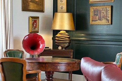 Façade d'une grande maison en pierre claire avec volets bleus, entourée d'un jardin et d'une allée gravillonnée.