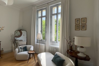 Façade d'une grande maison en pierre claire avec volets bleus, entourée d'un jardin et d'une allée gravillonnée.