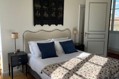 Façade d'une grande maison en pierre claire avec volets bleus, entourée d'un jardin et d'une allée gravillonnée.