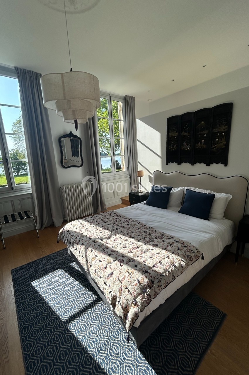 Chambre lumineuse avec lit double, grande fenêtre donnant sur un paysage verdoyant et décoration élégante.