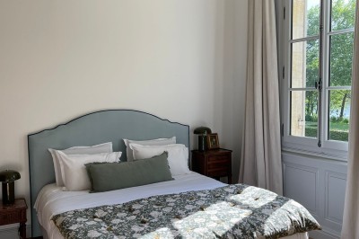 Façade d'une grande maison en pierre claire avec volets bleus, entourée d'un jardin et d'une allée gravillonnée.