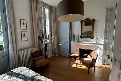 Façade d'une grande maison en pierre claire avec volets bleus, entourée d'un jardin et d'une allée gravillonnée.