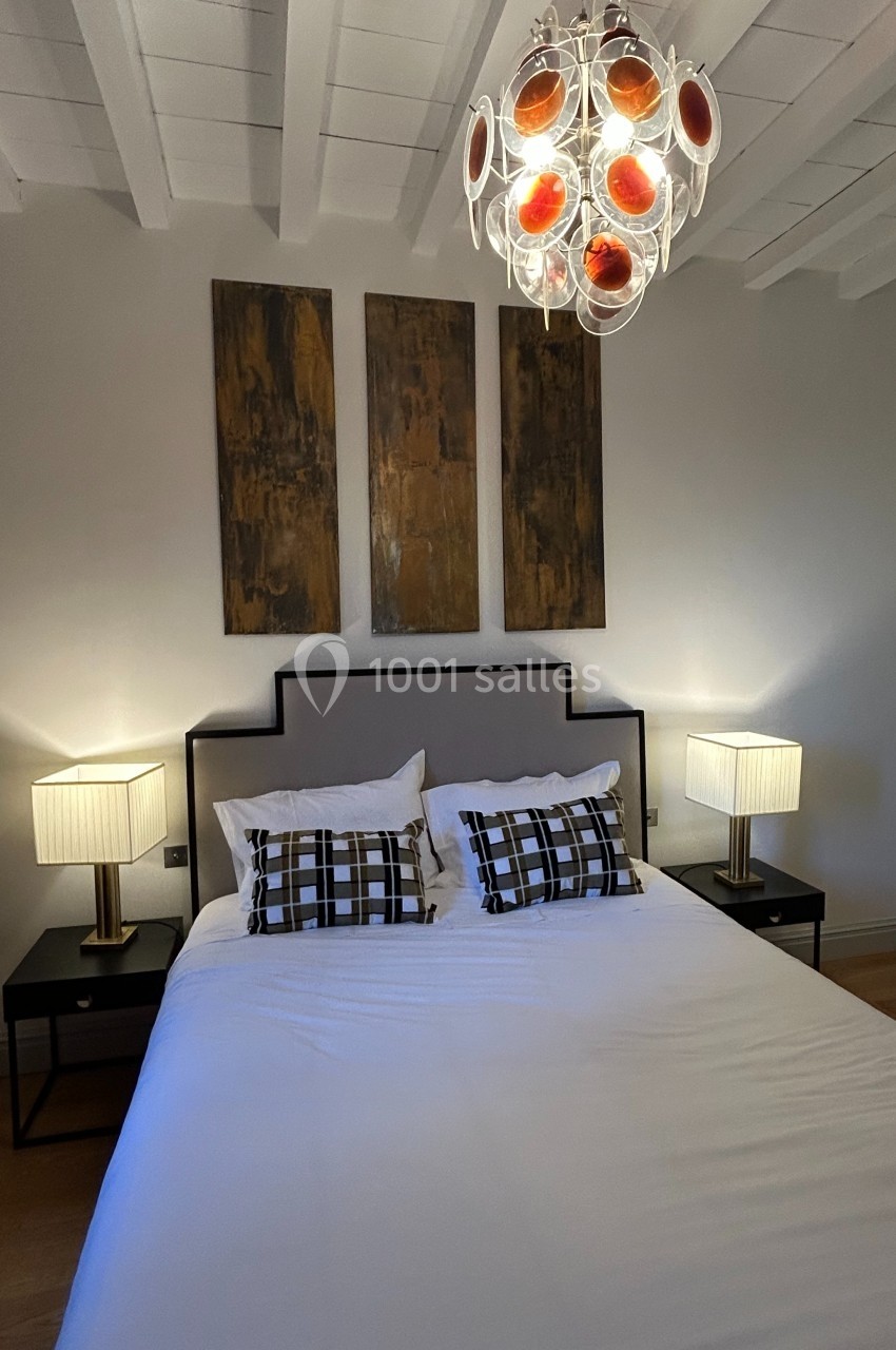 Lit double avec coussins à motifs, deux lampes de chevet, tableau mural et suspension lumineuse moderne.