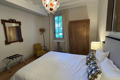 Façade d'une grande maison en pierre claire avec volets bleus, entourée d'un jardin et d'une allée gravillonnée.