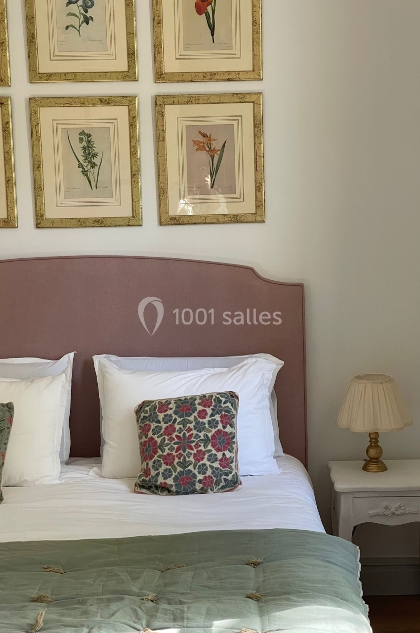 Lit avec tête de lit rose, coussins à motifs floraux, couvertures vertes et table de chevet avec lampe, décoré de cadres…