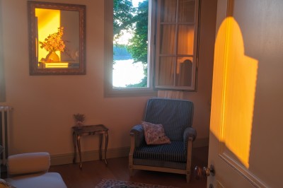 Façade d'une grande maison en pierre claire avec volets bleus, entourée d'un jardin et d'une allée gravillonnée.