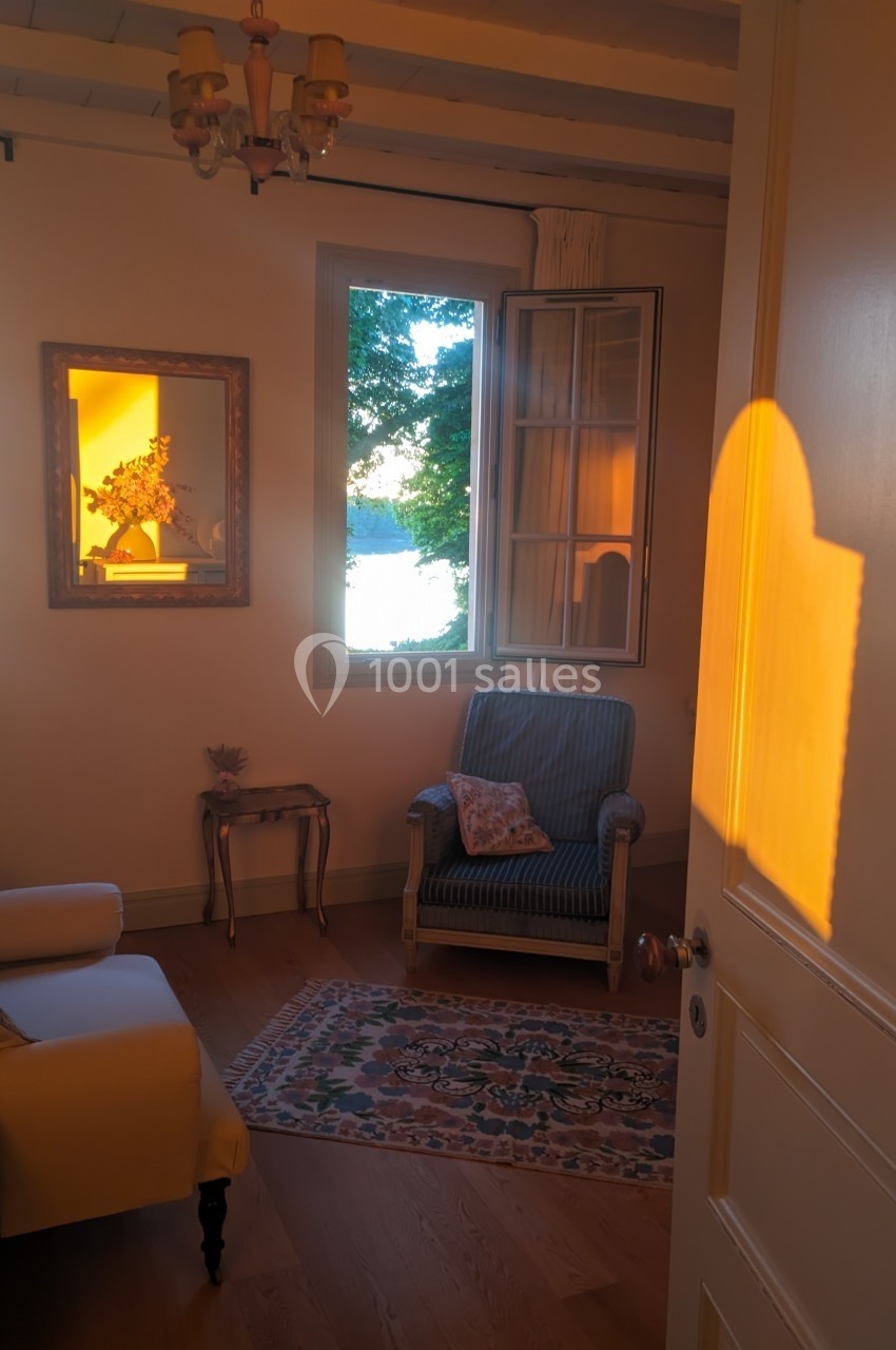 Salon chaleureux avec fauteuil, tapis et lumière dorée du soleil couchant entrant par une fenêtre ouverte.