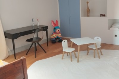 Façade d'une grande maison en pierre claire avec volets bleus, entourée d'un jardin et d'une allée gravillonnée.