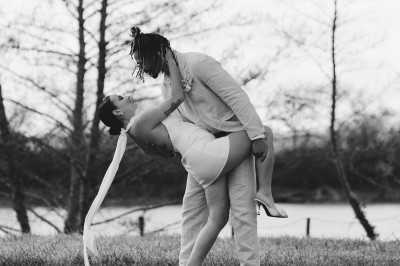 Façade d'une grande maison en pierre claire avec volets bleus, entourée d'un jardin et d'une allée gravillonnée.