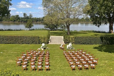 Façade d'une grande maison en pierre claire avec volets bleus, entourée d'un jardin et d'une allée gravillonnée.
