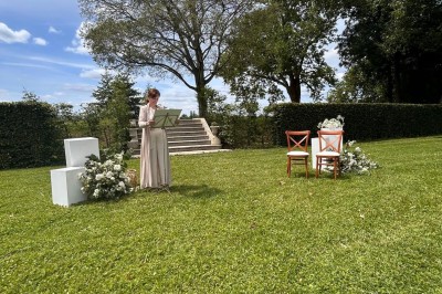 Façade d'une grande maison en pierre claire avec volets bleus, entourée d'un jardin et d'une allée gravillonnée.