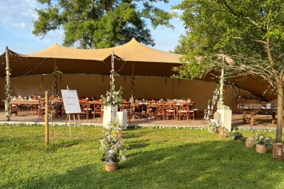 Façade d'une grande maison en pierre claire avec volets bleus, entourée d'un jardin et d'une allée gravillonnée.