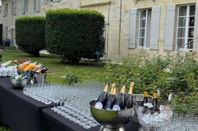 Façade d'une grande maison en pierre claire avec volets bleus, entourée d'un jardin et d'une allée gravillonnée.