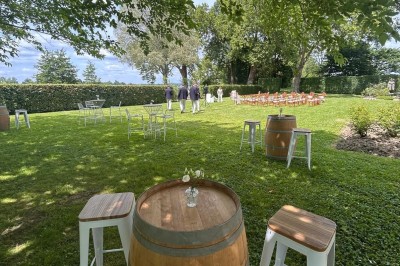 Façade d'une grande maison en pierre claire avec volets bleus, entourée d'un jardin et d'une allée gravillonnée.