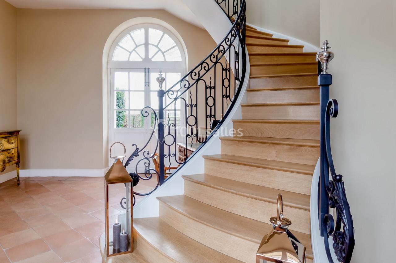 Escalier en bois courbé avec rampe en fer forgé, éclairé par une grande fenêtre et décoré de lanternes au sol.