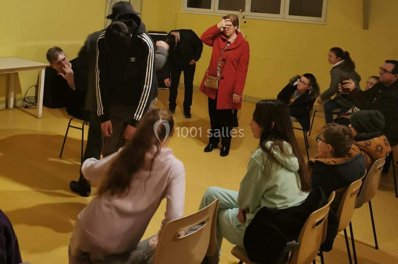 Des personnes assises et debout dans une salle jaune, certaines discutant ou interagissant entre elles.