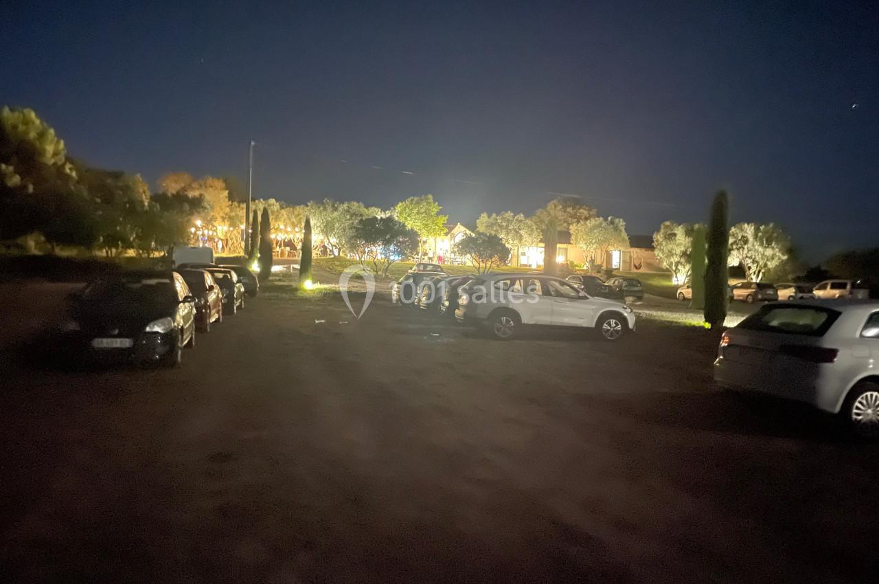 Parking extérieur de nuit avec plusieurs voitures alignées, éclairé par des lumières provenant d'un bâtiment au fond.