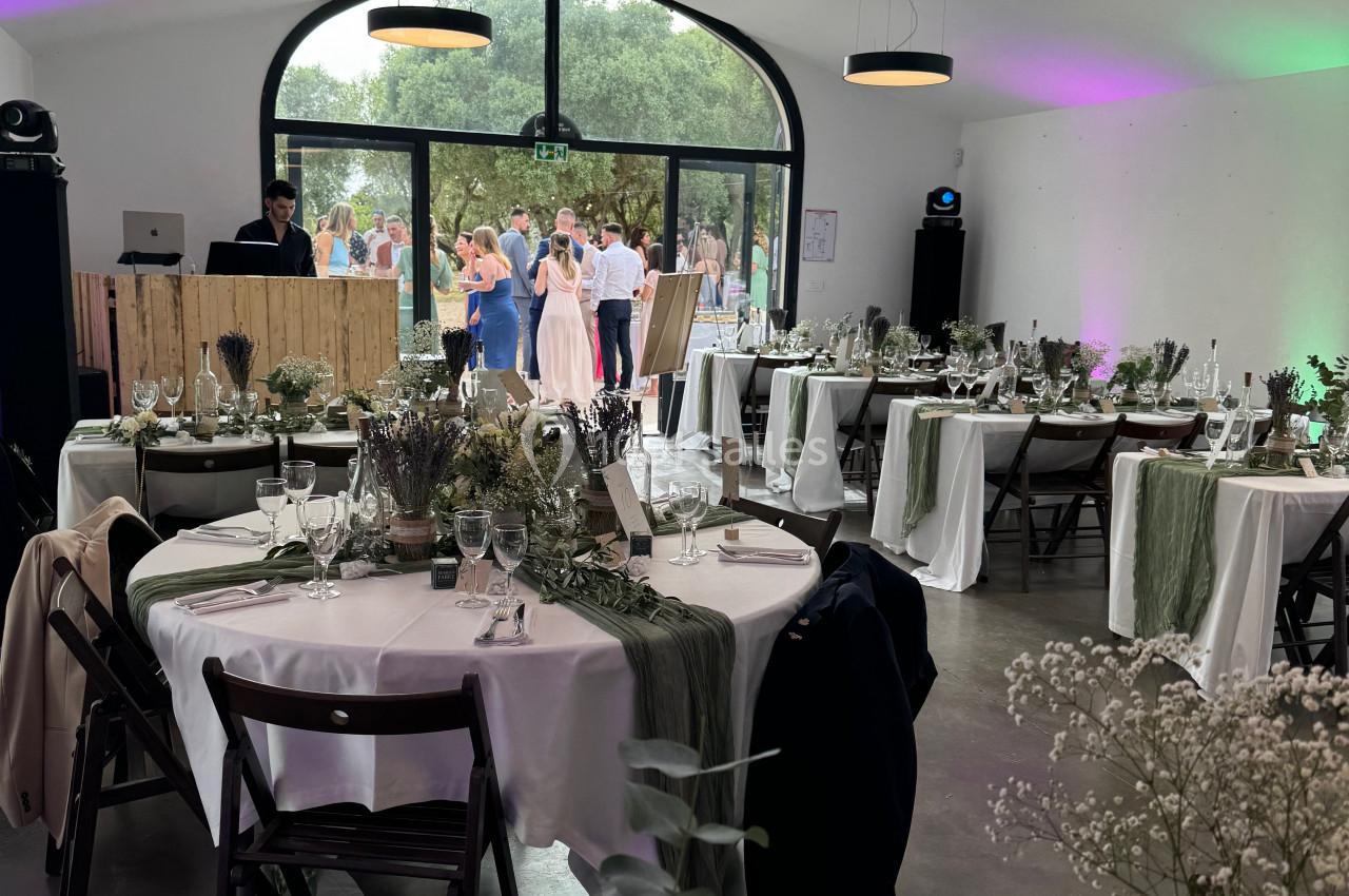 Salle de réception décorée avec des tables dressées, des nappes blanches et des invités dansant en arrière-plan.