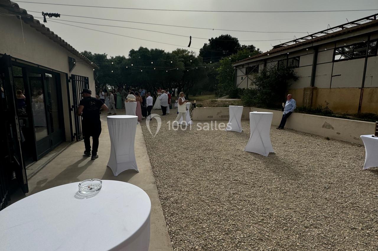 Personnes rassemblées dans une cour extérieure ensoleillée avec des tables hautes recouvertes de nappes blanches.