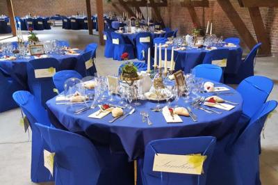 Salle de réception avec tables rondes dressées, décorées de rubans colorés et éclairée par des lustres en bois.