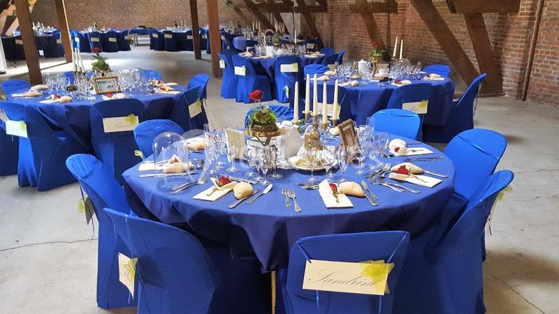 Tables rondes dressées avec nappes bleues, couverts élégants, chandeliers et décorations florales dans une grande salle en…