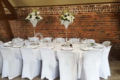 Salle de réception avec tables rondes dressées, décorées de rubans colorés et éclairée par des lustres en bois.