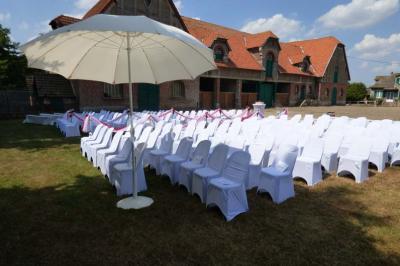 Salle de réception avec tables rondes dressées, décorées de rubans colorés et éclairée par des lustres en bois.