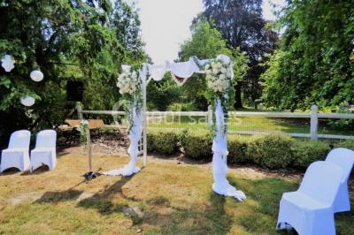 Salle de réception avec tables rondes dressées, décorées de rubans colorés et éclairée par des lustres en bois.