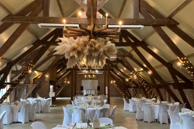 Salle de réception avec tables rondes dressées, décorées de rubans colorés et éclairée par des lustres en bois.