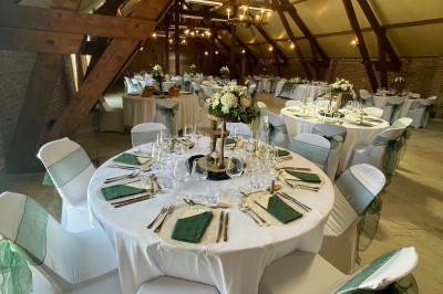 Salle de réception avec tables rondes dressées, décorées de rubans colorés et éclairée par des lustres en bois.
