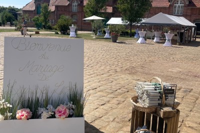 Salle de réception avec tables rondes dressées, décorées de rubans colorés et éclairée par des lustres en bois.