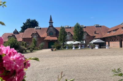 Salle de réception avec tables rondes dressées, décorées de rubans colorés et éclairée par des lustres en bois.