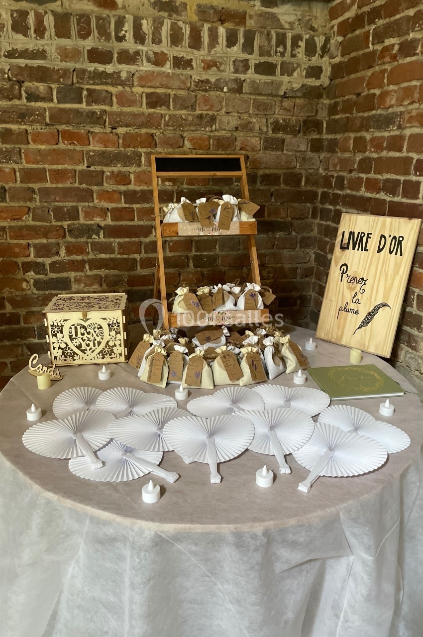 Table décorée pour un événement avec éventails blancs, bougies, boîte en bois et présentoir de cadeaux devant un mur en…