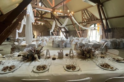 Salle de réception avec tables rondes dressées, décorées de rubans colorés et éclairée par des lustres en bois.