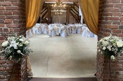 Salle de réception avec tables rondes dressées, décorées de rubans colorés et éclairée par des lustres en bois.