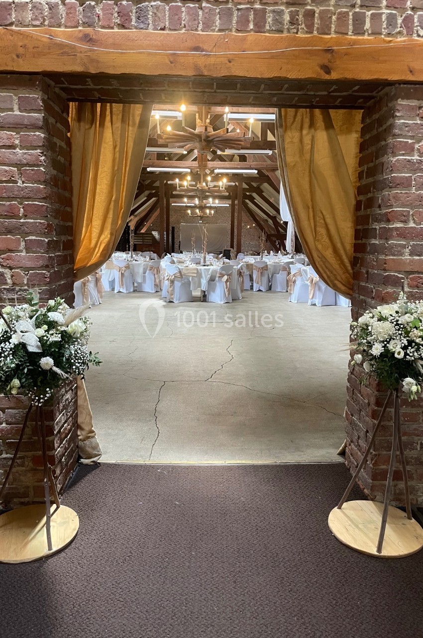 Entrée d'une salle de réception décorée avec des fleurs blanches, des rideaux dorés et des tables dressées.