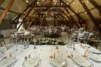 Salle de réception avec tables rondes dressées, décorées de rubans colorés et éclairée par des lustres en bois.