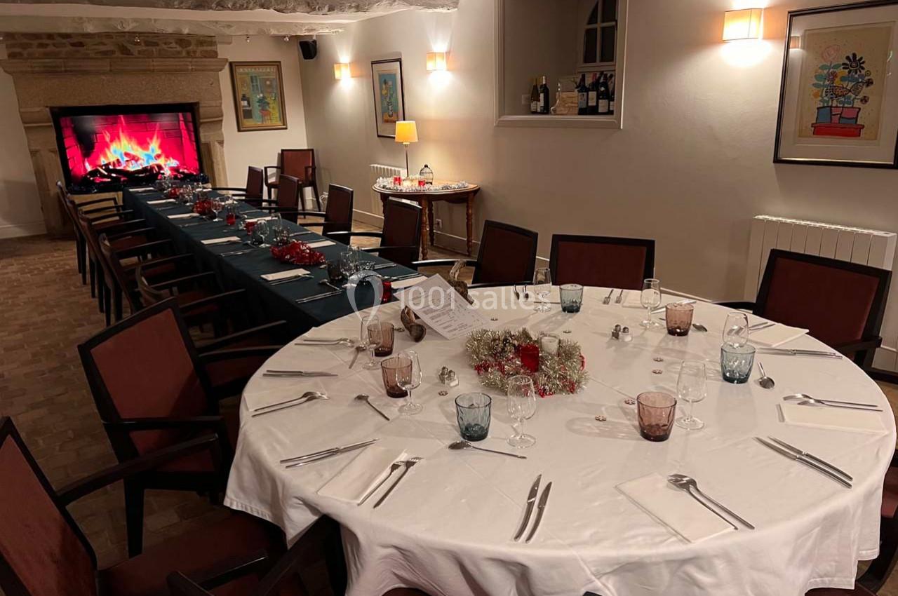 Salle à manger décorée pour un repas festif, avec une grande table ronde et une cheminée virtuelle allumée.