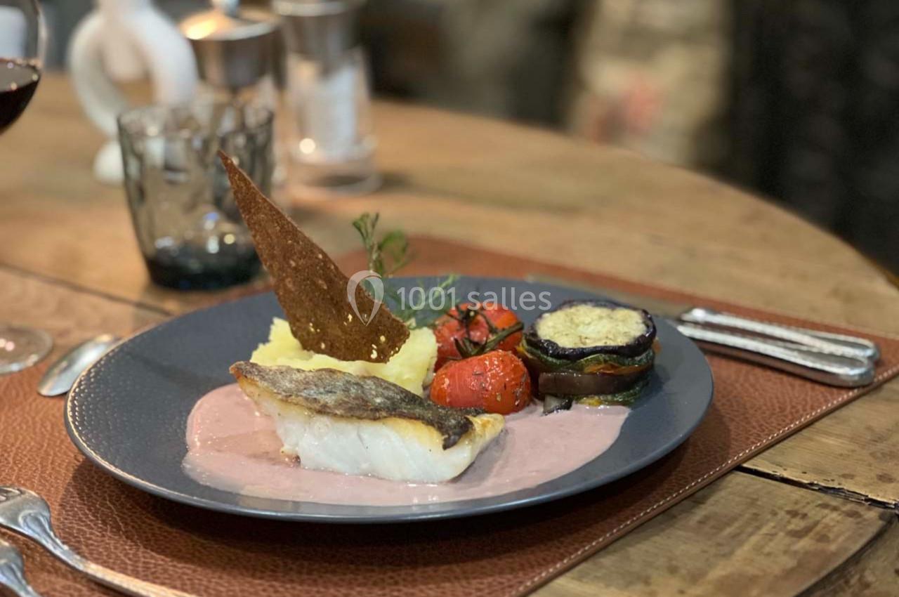 Assiette de poisson accompagné de purée, légumes grillés et sauce, servie sur une table en bois.