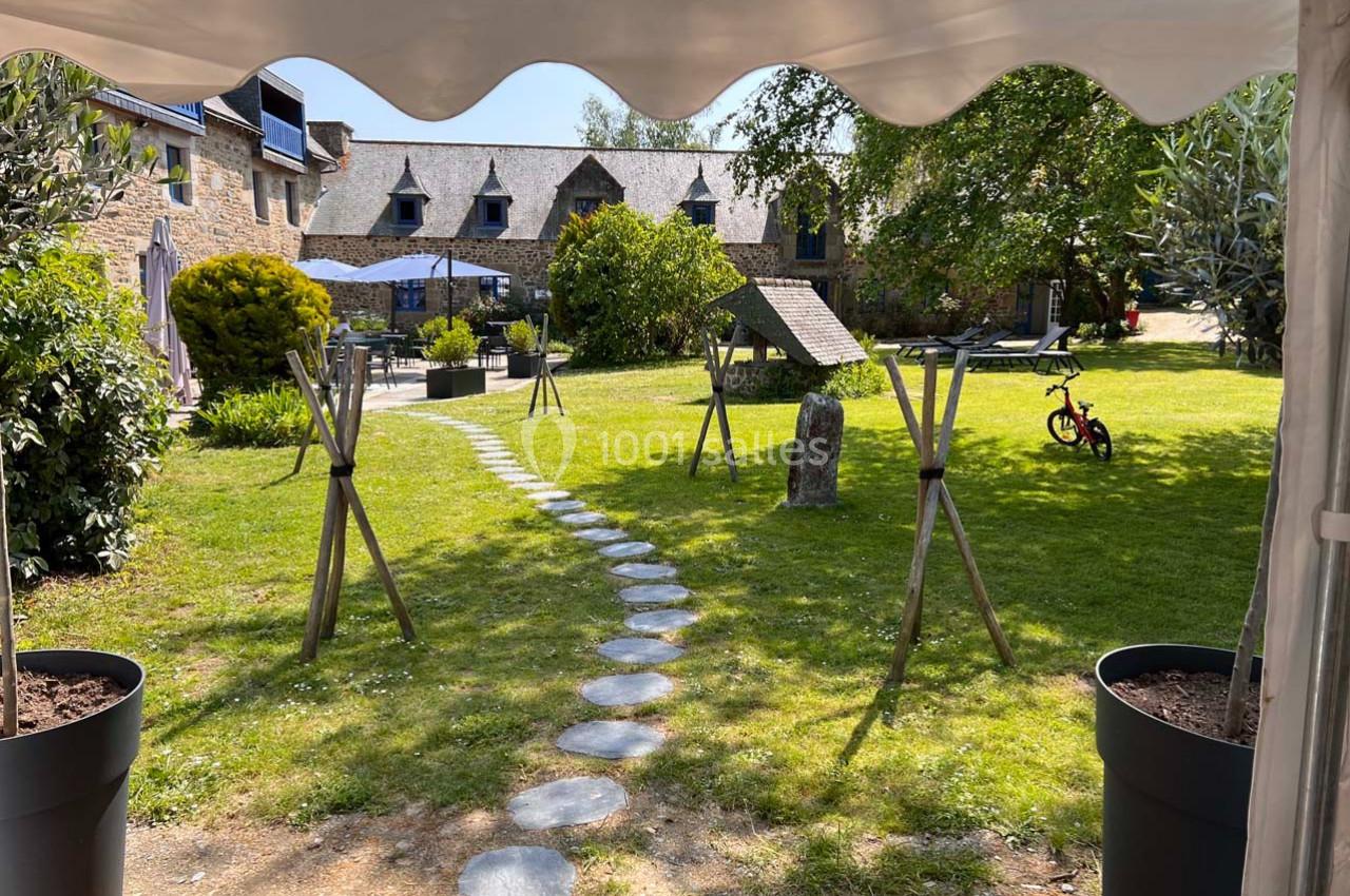 Jardin verdoyant avec un sentier en pierres menant à une maison en pierre, entouré d'arbres et de mobilier de jardin.