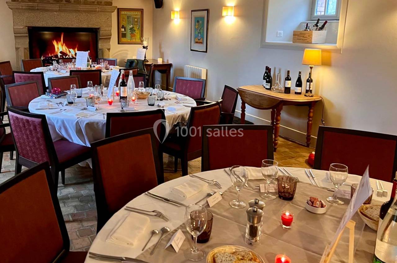 Salle de restaurant chaleureuse avec tables dressées, bougies allumées et cheminée en arrière-plan.
