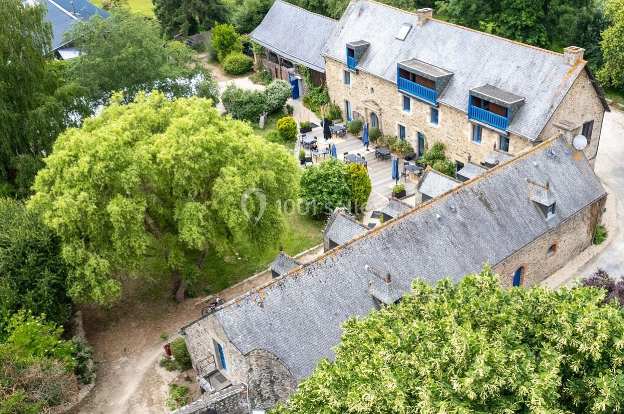 Vue aérienne d'un ensemble de bâtiments en pierre avec toits en ardoise, entouré de verdure et d'arbres.