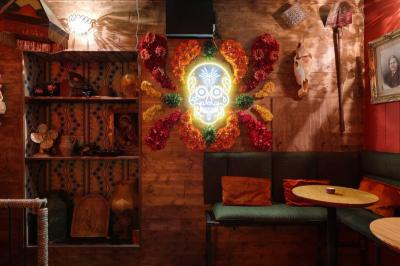 Intérieur d'un bar avec comptoir en métal, éclairage rouge, tables en bois et décorations murales éclectiques.