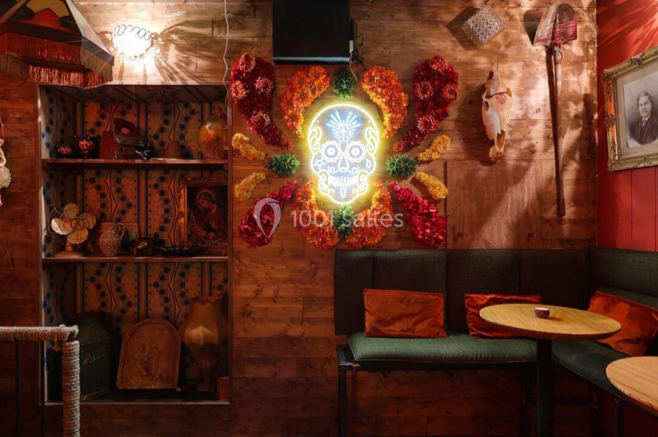 Décoration intérieure colorée avec un mur en bois, un néon en forme de crâne entouré de fleurs et des objets variés.