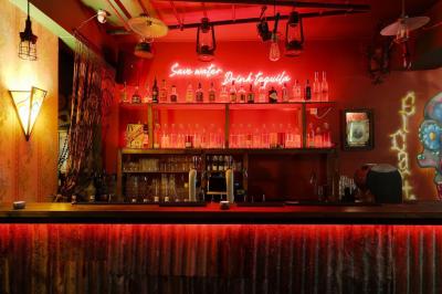Intérieur d'un bar avec comptoir en métal, éclairage rouge, tables en bois et décorations murales éclectiques.