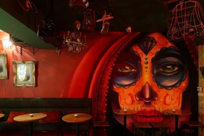 Intérieur d'un bar avec comptoir en métal, éclairage rouge, tables en bois et décorations murales éclectiques.