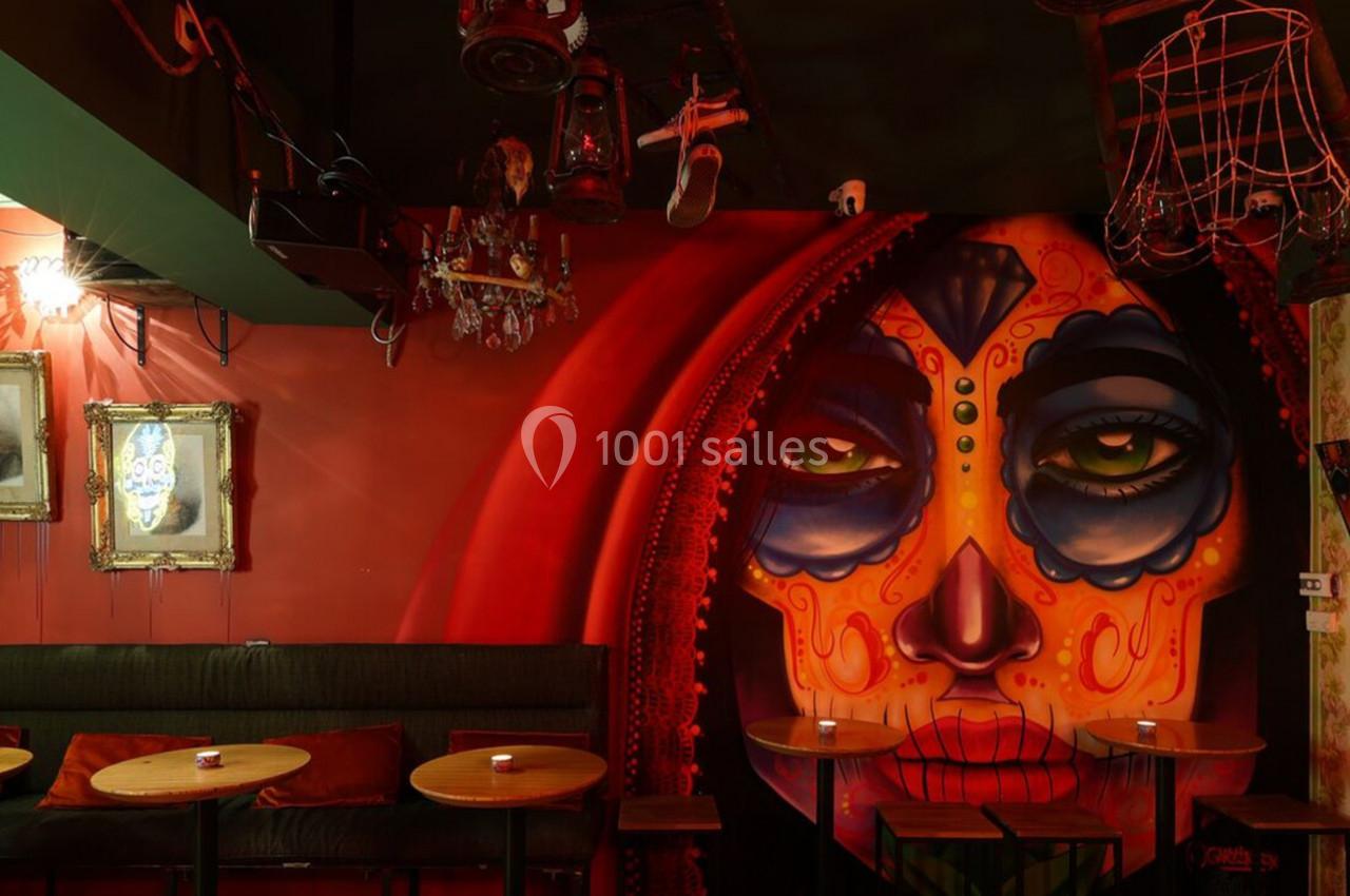 Fresque murale colorée représentant un visage féminin masqué, entourée de décorations éclectiques dans un bar sombre.