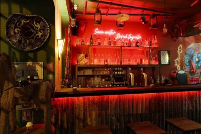 Intérieur d'un bar avec comptoir en métal, éclairage rouge, tables en bois et décorations murales éclectiques.