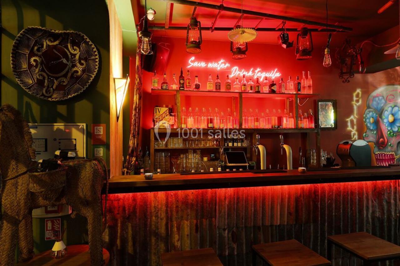 Bar à l'ambiance tamisée avec décorations colorées, étagères remplies de bouteilles et enseigne lumineuse au mur.